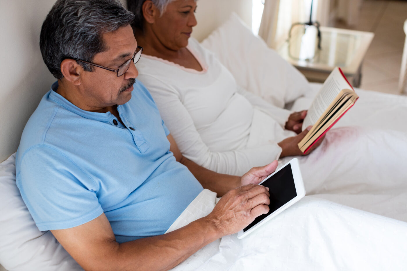 senior-woman-reading-a-novel-and-senior-man-using-2023-11-27-05-20-48-utc-1400x933